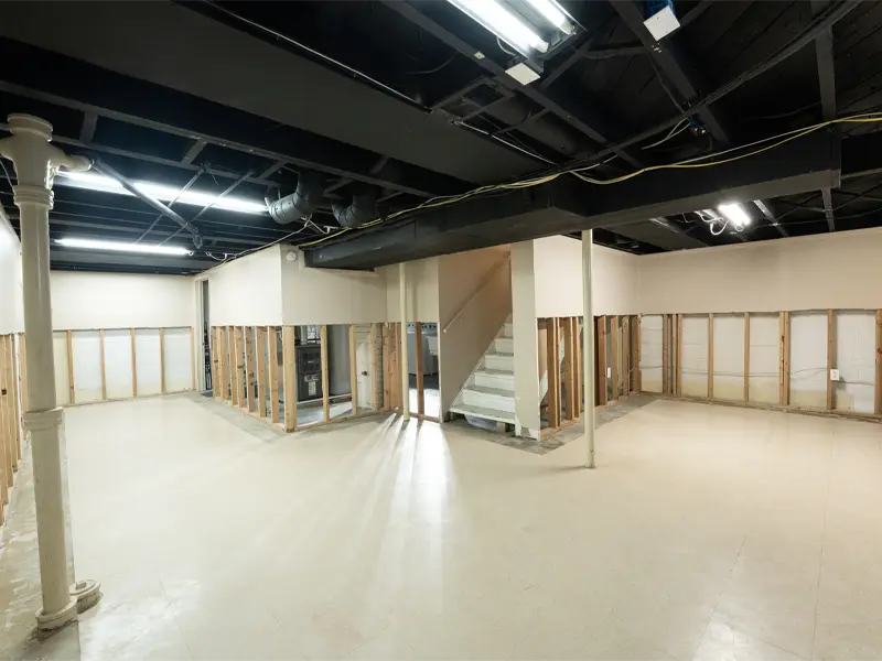 Basement with exposed wall studs, white tiled floor, and a staircase in the center. cleaned by a experienced restoration company in San Diego
