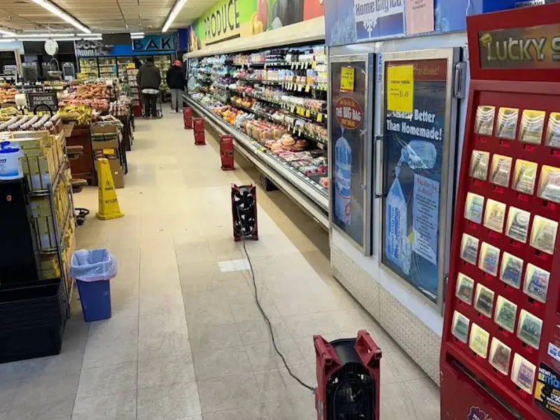 Fans placed on the floor of a grocery store aisle near refrigerated produce cases. commercial water damage restoration