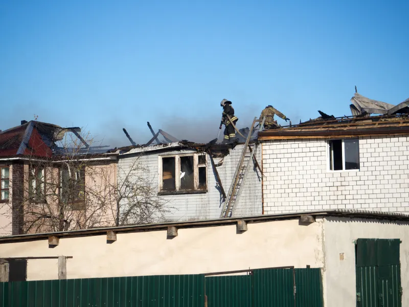 Firefighters on the roof of a damaged building with smoke rising in the background. fire damage restoration