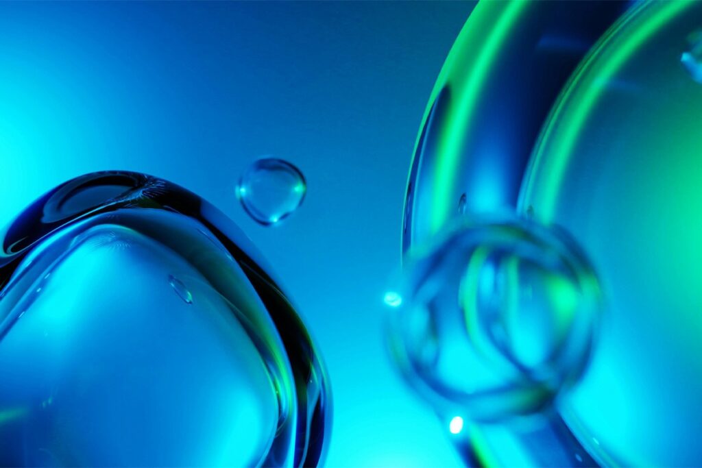 Close-up of translucent blue and green bubbles or liquid droplets against a gradient blue background.